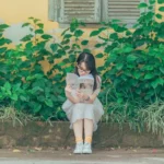 A girl sitting and reading a book with greenery background.