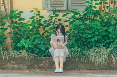A girl sitting and reading a book with greenery background.